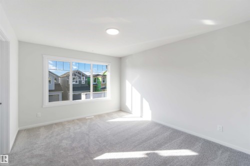 This room features light gray carpeting, a large window providing natural light, a ceiling light fixture, and light-colored walls - 18940 28 Avenue, Edmonton, AB - Indoor Photo Showing Other Room