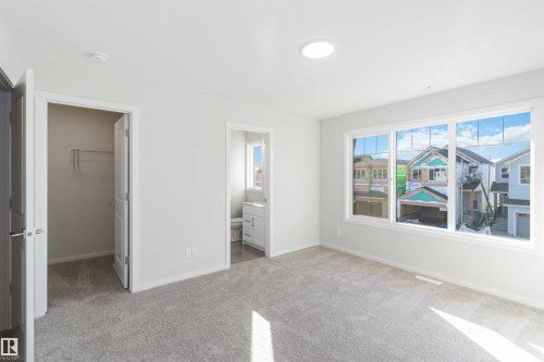 This property features a bright room with light grey carpet, white walls, and a large window offering ample natural light - 18940 28 Avenue, Edmonton, AB - Indoor Photo Showing Other Room