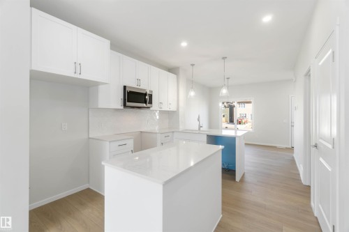 The kitchen features white cabinetry, a stainless steel microwave, and two islands with white countertops - 18940 28 Avenue, Edmonton, AB - Indoor Photo Showing Kitchen