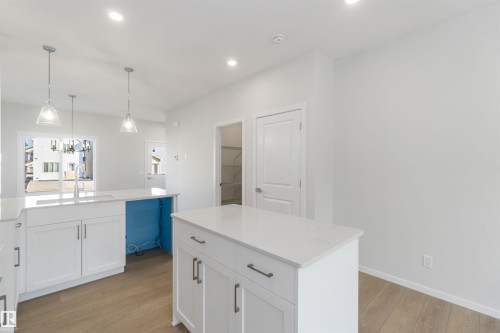 The kitchen features white cabinetry with dark hardware, light-colored countertops, and two islands - 18940 28 Avenue, Edmonton, AB - Indoor Photo Showing Kitchen
