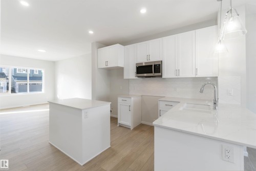 Modern kitchen featuring white cabinetry, light countertops, a stainless steel microwave, and a kitchen island - 18940 28 Avenue, Edmonton, AB - Indoor Photo Showing Kitchen