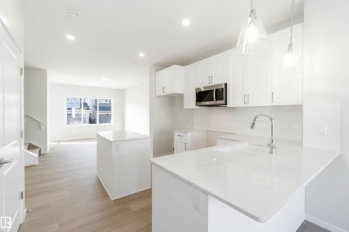 Modern kitchen featuring white cabinetry, a stainless steel microwave, and quartz countertops with an integrated sink and chrome faucet - 18940 28 Avenue, Edmonton, AB - Indoor Photo Showing Kitchen