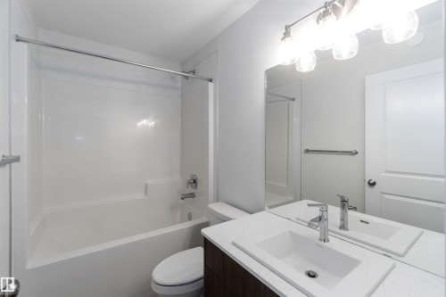 The bathroom features a vanity with a rectangular sink, a polished chrome faucet, and a large mirror with a four-light fixture - 5452 Hawthorn Run, Edmonton, AB - Indoor Photo Showing Bathroom