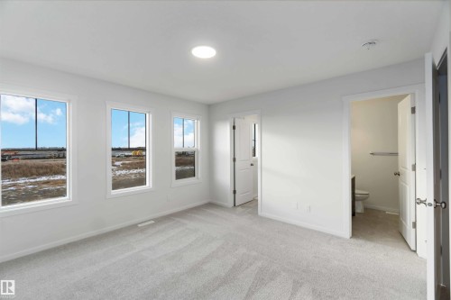 Spacious room featuring light-colored walls, carpeted flooring, and three windows providing ample natural light - 5452 Hawthorn Run, Edmonton, AB - Indoor Photo Showing Other Room