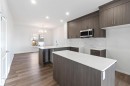 The kitchen features dark wood cabinetry, white countertops, and a white marble-style backsplash, complemented by a stainless steel microwave - 5452 Hawthorn Run, Edmonton, AB  - Indoor Photo Showing Kitchen With Upgraded Kitchen 