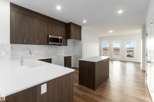 The kitchen features dark wood cabinetry, white countertops, a stainless steel microwave, and a white tile backsplash - 5452 Hawthorn Run, Edmonton, AB - Indoor Photo Showing Kitchen
