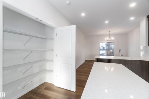 The kitchen features a white countertop island, a sink with a stainless steel faucet, and dark wood cabinetry - 5452 Hawthorn Run, Edmonton, AB - Indoor