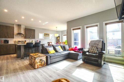 Open concept living area featuring light-toned flooring, a kitchen with dark cabinetry and light countertops, and large windows that provide natural light - 20503 99 Avenue, Edmonton, AB - Indoor Photo Showing Living Room
