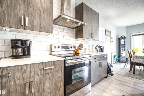 The kitchen features wood grain cabinetry, a white subway tile backsplash, and a stainless steel range with an overhead exhaust fan - 20503 99 Avenue, Edmonton, AB - Indoor Photo Showing Kitchen With Upgraded Kitchen