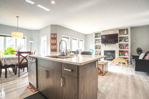 Open concept living area featuring light-toned flooring, a kitchen island with a sink and dishwasher, and a living room with a fireplace and built-in shelving - 20503 99 Avenue, Edmonton, AB - Indoor With Fireplace