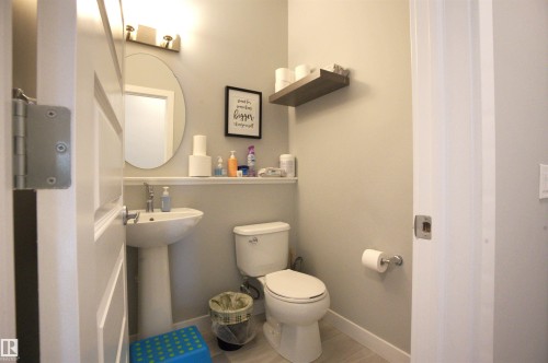 This bathroom features a pedestal sink, a toilet, an oval mirror, and a wall-mounted light fixture - 20503 99 Avenue, Edmonton, AB - Indoor Photo Showing Bathroom