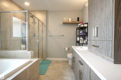 The bathroom features a glass-enclosed shower with tile surround, a built-in bathtub, and a double vanity with light-colored cabinetry and white countertops - 20503 99 Avenue, Edmonton, AB - Indoor Photo Showing Bathroom
