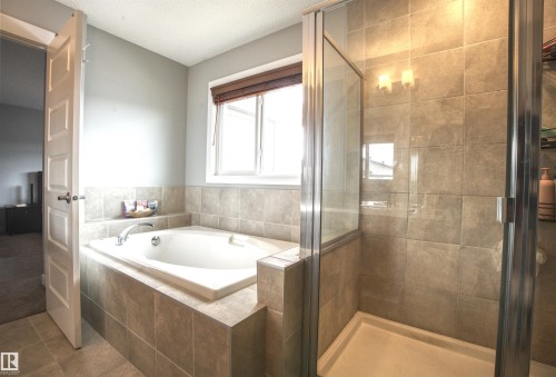 Bathroom featuring a tiled shower enclosure with a glass door, a separate bathtub with tile surround, and a window with blinds - 20503 99 Avenue, Edmonton, AB - Indoor Photo Showing Bathroom