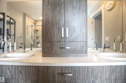 Bathroom featuring a double vanity with two undermount sinks, a light-colored countertop, and a centrally located storage cabinet with drawers - 20503 99 Avenue, Edmonton, AB - Indoor Photo Showing Bathroom