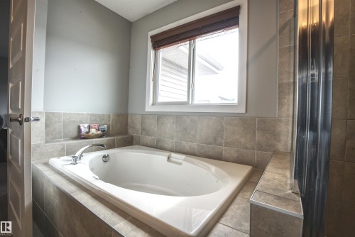 Soaking tub with tiled surround, a window featuring blinds, and a chrome faucet - 20503 99 Avenue, Edmonton, AB - Indoor Photo Showing Bathroom