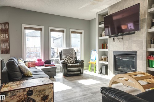 Living area featuring large windows, light-colored flooring, a tiled fireplace, and built-in shelving - 20503 99 Avenue, Edmonton, AB - Indoor Photo Showing Living Room With Fireplace