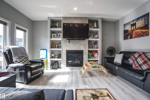 Living room featuring light-colored flooring, a fireplace with a tiled surround, built-in shelving, and large windows providing natural light - 20503 99 Avenue, Edmonton, AB - Indoor Photo Showing Living Room With Fireplace