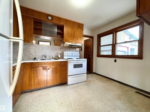 The kitchen features wood cabinetry, a white electric range, and a dual basin sink with mosaic tile backsplash - 12219 48 Street, Edmonton, AB - Indoor Photo Showing Kitchen With Double Sink
