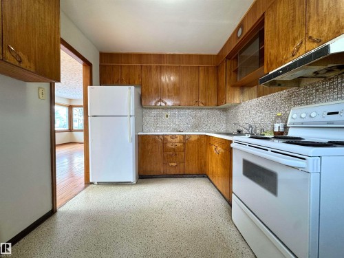 The kitchen features wood cabinetry, a mosaic tile backsplash, and a white oven and refrigerator - 12219 48 Street, Edmonton, AB - Indoor Photo Showing Kitchen