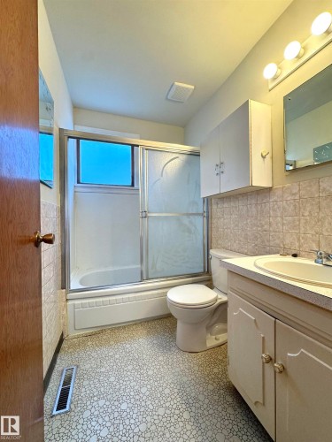 Bathroom featuring a bathtub with a sliding glass door, a toilet, a vanity with a sink, and tiled walls - 12219 48 Street, Edmonton, AB - Indoor Photo Showing Bathroom