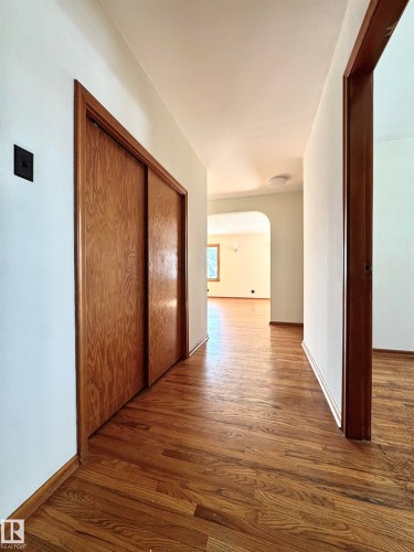 This hallway features hardwood flooring and light-colored walls, leading into an arched entryway - 12219 48 Street, Edmonton, AB - Indoor Photo Showing Other Room