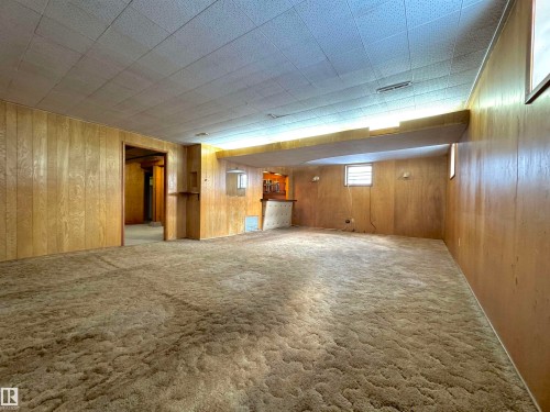 Spacious room featuring paneled walls, a drop ceiling, and carpeted flooring - 12219 48 Street, Edmonton, AB - Indoor