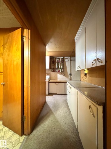 This room features wood paneled walls, a carpeted floor, and white cabinetry with brass-toned hardware - 12219 48 Street, Edmonton, AB - Indoor Photo Showing Kitchen