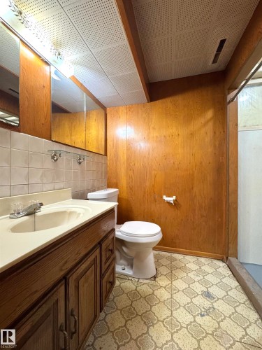 This bathroom features a wood vanity with a white countertop and an integrated sink, complemented by a large mirror with overhead lighting - 12219 48 Street, Edmonton, AB - Indoor Photo Showing Bathroom