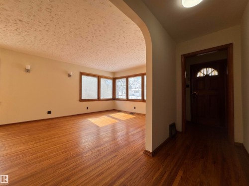 The property features hardwood floors, a bay window, and a wood door with an arched window - 12219 48 Street, Edmonton, AB - Indoor Photo Showing Other Room