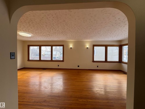 This spacious interior features hardwood floors, light-colored walls, and a ceiling light fixture - 12219 48 Street, Edmonton, AB - Indoor Photo Showing Other Room