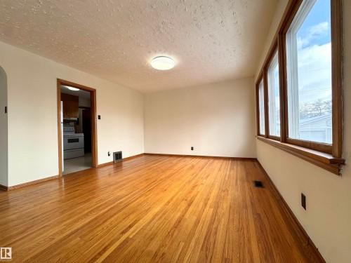 This living area features polished hardwood floors and large windows with wooden frames, allowing for abundant natural light - 12219 48 Street, Edmonton, AB - Indoor Photo Showing Other Room