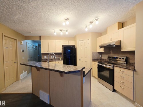 The kitchen features light-colored cabinetry and a central island with a sink and a dark countertop - 60 1128 156 Street, Edmonton, AB - Indoor Photo Showing Kitchen
