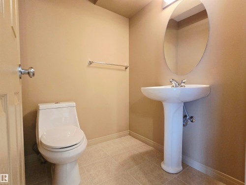 This bathroom features a white pedestal sink with a chrome faucet, a white toilet, and an oval mirror with overhead lighting - 60 1128 156 Street, Edmonton, AB - Indoor Photo Showing Bathroom