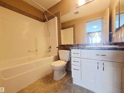 The ensuite features a combined shower and bathtub, a white vanity with a dark countertop, and linoleum flooring - 60 1128 156 Street, Edmonton, AB - Indoor Photo Showing Bathroom
