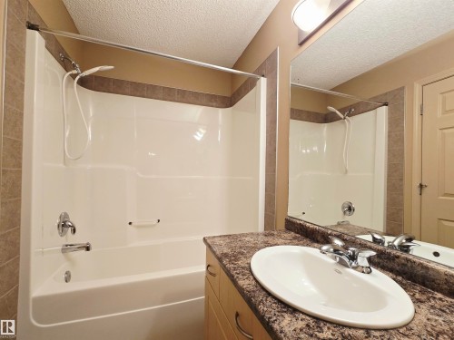 Bathroom featuring a vanity with an oval sink, a mirror, and a bathtub with an integrated shower, and linoleum flooring - 60 1128 156 Street, Edmonton, AB - Indoor Photo Showing Bathroom