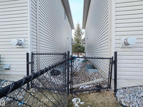 The property features light-colored horizontal siding and a black chain link fence - 60 1128 156 Street, Edmonton, AB - Outdoor With Exterior