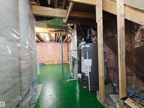The property features a utility area with exposed wooden joists, a water heater, and a green painted floor - 60 1128 156 Street, Edmonton, AB - Indoor Photo Showing Basement