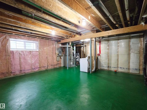 Spacious unfinished basement offering a large green painted concrete floor, exposed wooden ceiling beams, and a window providing natural light - 60 1128 156 Street, Edmonton, AB - Indoor Photo Showing Basement
