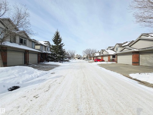 Complex driveway view featuring properties with attached garages and brick accents - 60 1128 156 Street, Edmonton, AB - Outdoor With Facade