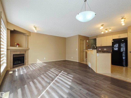 Open concept living space featuring newer laminated flooring, a fireplace with a tiled surround, and a kitchen area with a black refrigerator, light-colored cabinetry, and a bar-height counter - 60 1128 156 Street, Edmonton, AB - Indoor With Fireplace