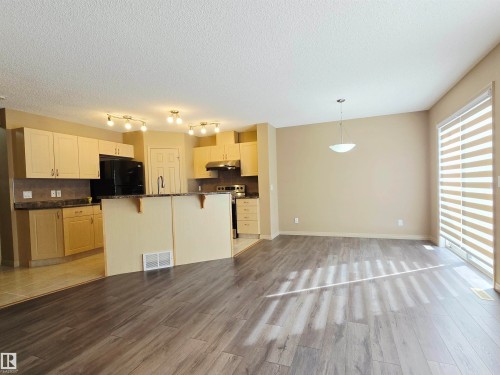The open concept living area features newer laminated flooring and a sliding glass door with horizontal blinds - 60 1128 156 Street, Edmonton, AB - Indoor Photo Showing Kitchen