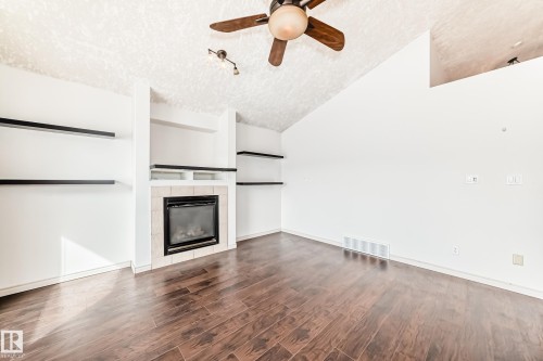 Living area featuring a fireplace with tile surround, built-in shelving, rich wood-look flooring, and a ceiling fan - 10631 181 Avenue, Edmonton, AB - Indoor Photo Showing Other Room With Fireplace