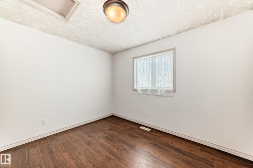 This room features warm-toned wood flooring, a window with white trim, and a ceiling light fixture - 10631 181 Avenue, Edmonton, AB - Indoor Photo Showing Other Room