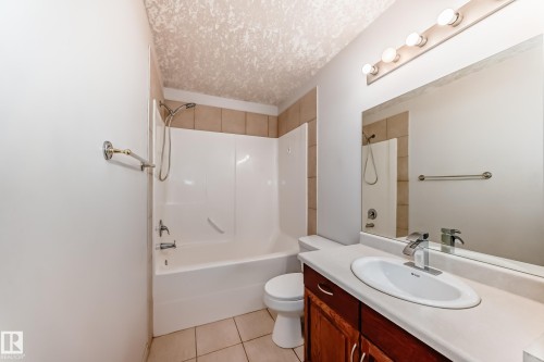 Well-maintained bathroom featuring a vanity with a white countertop and wood cabinetry, a large mirror, and a bathtub with an integrated shower - 10631 181 Avenue, Edmonton, AB - Indoor Photo Showing Bathroom