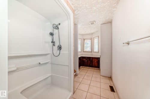 The bathroom features a white shower enclosure with a built-in seat and grab bars, a chrome showerhead with a handheld sprayer, and tiled flooring - 10631 181 Avenue, Edmonton, AB - Indoor Photo Showing Bathroom