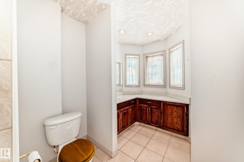 The bathroom features a toilet with a wooden seat, tiled flooring, and a vanity with rich wooden cabinetry and a light-colored countertop - 10631 181 Avenue, Edmonton, AB - Indoor Photo Showing Bathroom
