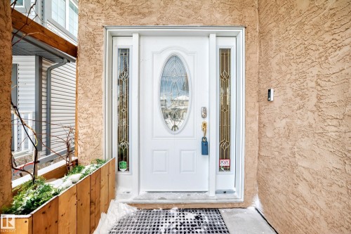 The property features a white front door with an oval glass insert and decorative side panels, set against a textured exterior wall - 10631 181 Avenue, Edmonton, AB - Outdoor With Exterior