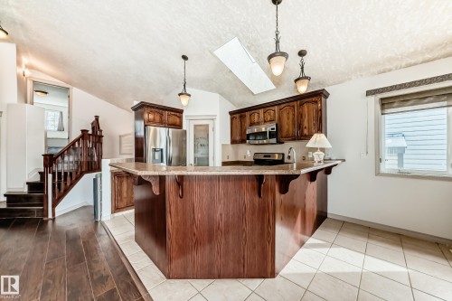 The kitchen features a breakfast bar with wood cabinetry, stainless steel appliances, and pendant lighting - 10631 181 Avenue, Edmonton, AB - Indoor Photo Showing Kitchen