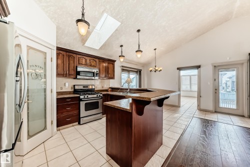 The kitchen features a pantry with a frosted glass door, stainless steel appliances, and a breakfast bar with a stone countertop - 10631 181 Avenue, Edmonton, AB - Indoor Photo Showing Kitchen With Upgraded Kitchen