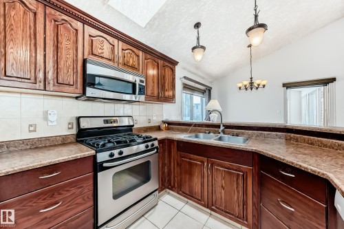 The kitchen features wood cabinetry, stainless steel appliances, a double basin sink, and a tiled backsplash - 10631 181 Avenue, Edmonton, AB - Indoor Photo Showing Kitchen With Double Sink